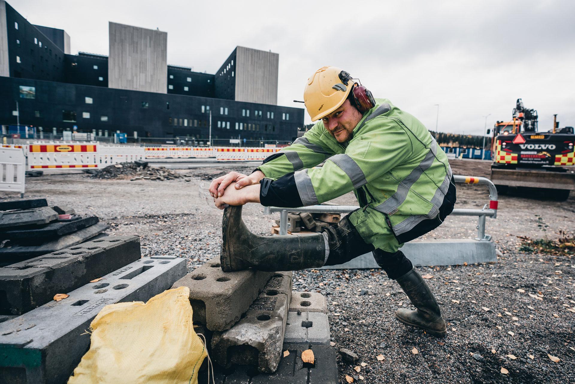 A builder stretches his leg on a construction site.