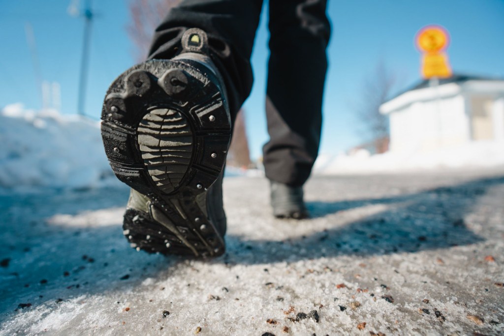 Kuvassa näkyvät nastapohjaiset kengät talvisella hiekoitetulla kävelytiellä.