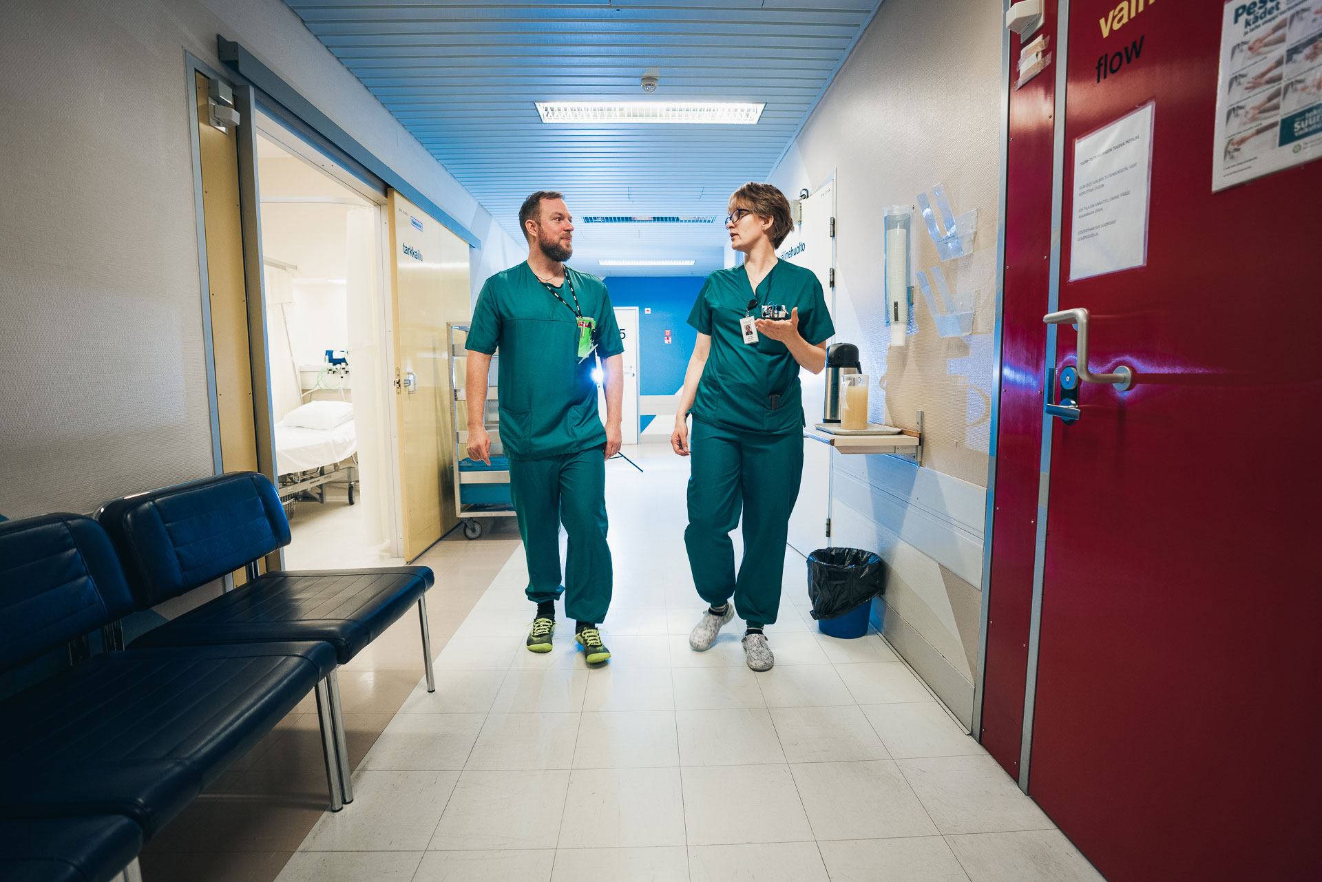 Kuvassa hoitohenkilöstöön kuuluva mies ja nainen kävelevät sairaalan käytävällä.
