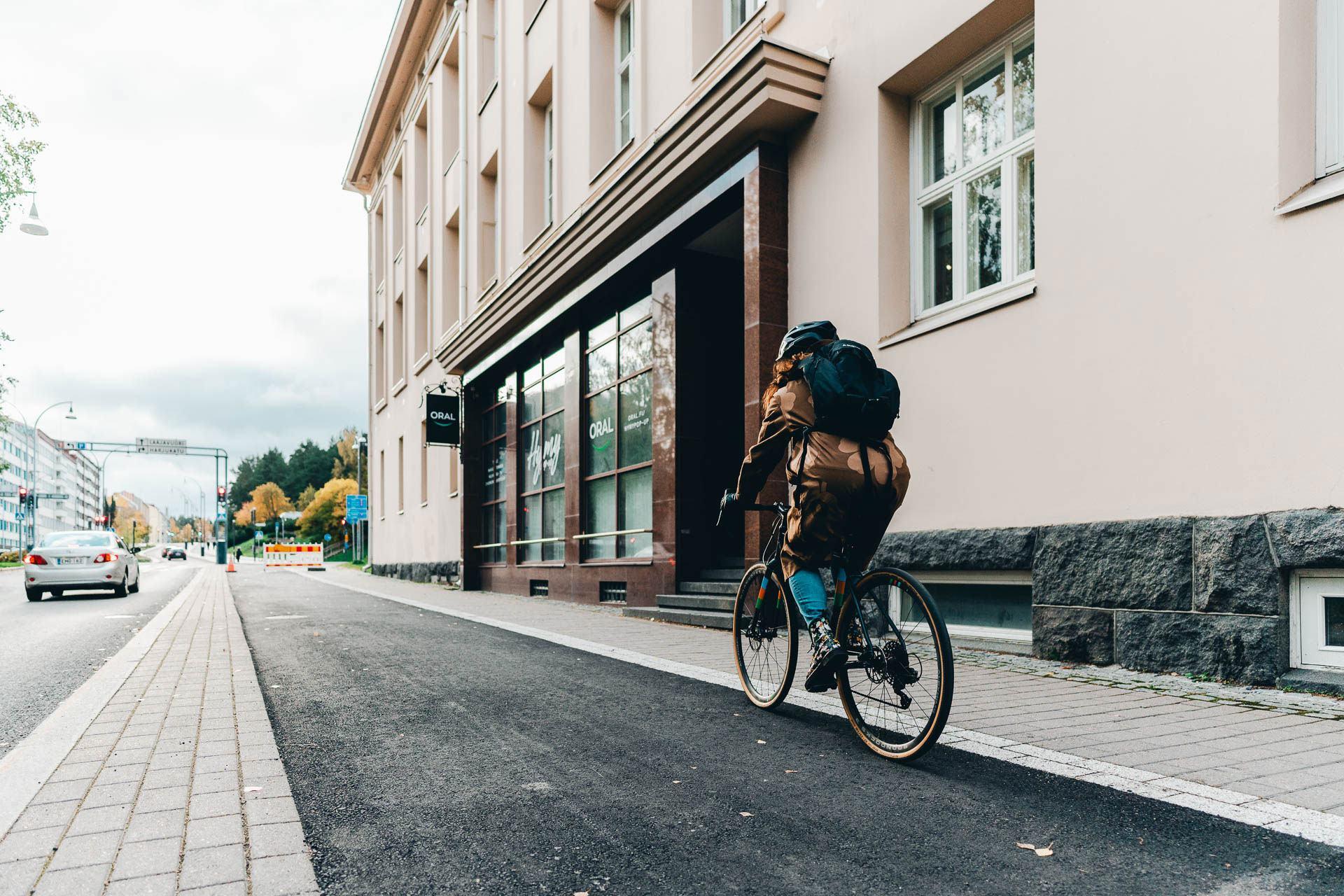 Kuvassa nainen polkee polkupyörällä kaupungin kadulla.