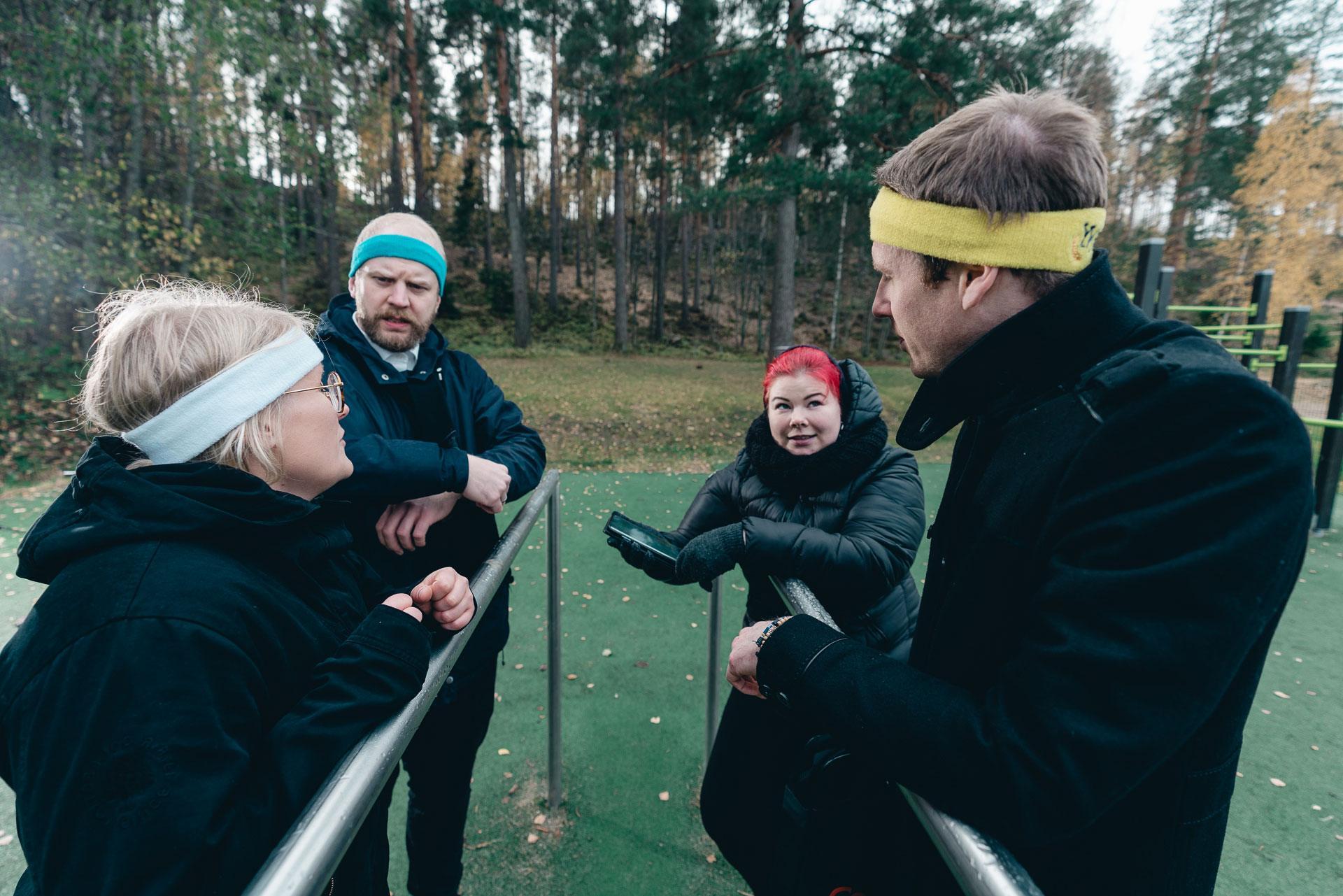 Kuvassa on neljä henkilöä hikinauhat päässään ulkokuntosalilaitteen äärellä.