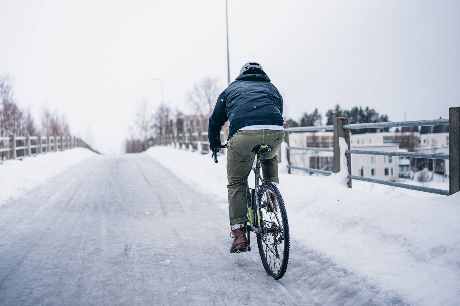 Kuvassa henkilö ajaa polkupyörällä talvisessa maisemassa sillalla.