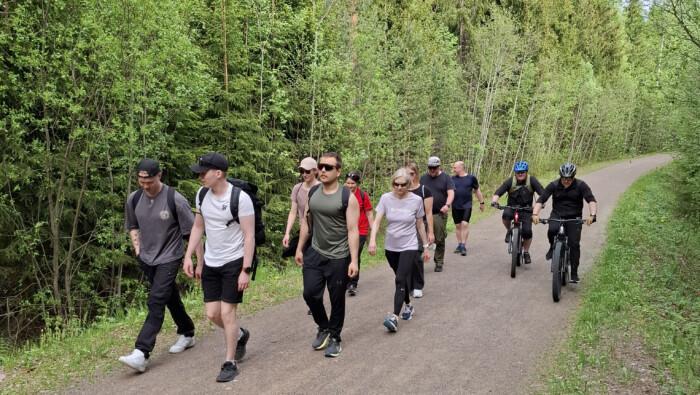 Kuvassa työporukka kävelemässä ja pyöräilemässä metsätiellä.