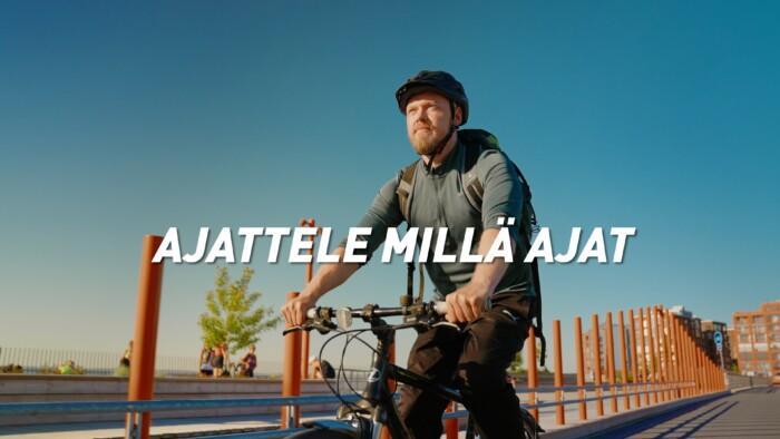 Kuvassa on pyöräilevä mies kaupunkimaisemassa. Kuvan päällä on teksti Ajattele millä ajat.