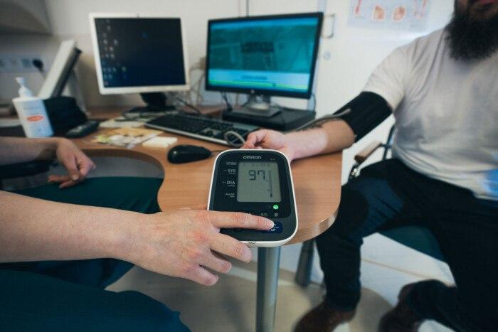 Kuvassa näkyy työpöydälle asetettu verenpainemittari sekä kahden ihmisen kädet.